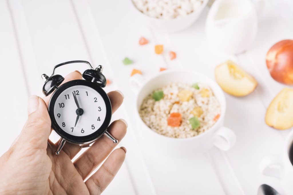 mano de una persona que sostiene el despertador en mano sobre el desayuno en la mesa
