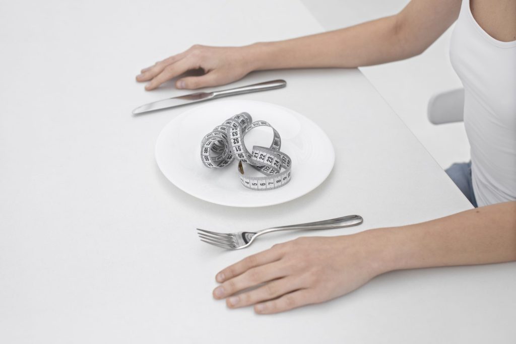 mujer joven con un trastorno alimentario con una cinta metrica en el plato